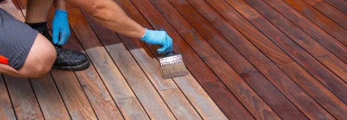 Person streicht Holzboden mit Pinsel